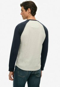 Camisa raglán de manga larga con cuerpo gris claro y mangas azul oscuro, hecha de un tejido suave con un corte relajado y costuras en contraste.