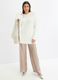 Maglione bianco in peluche abbinato a pantaloni larghi in satin beige chiaro e tacchi a punta metallici, creando un look stratificato e testurizzato.