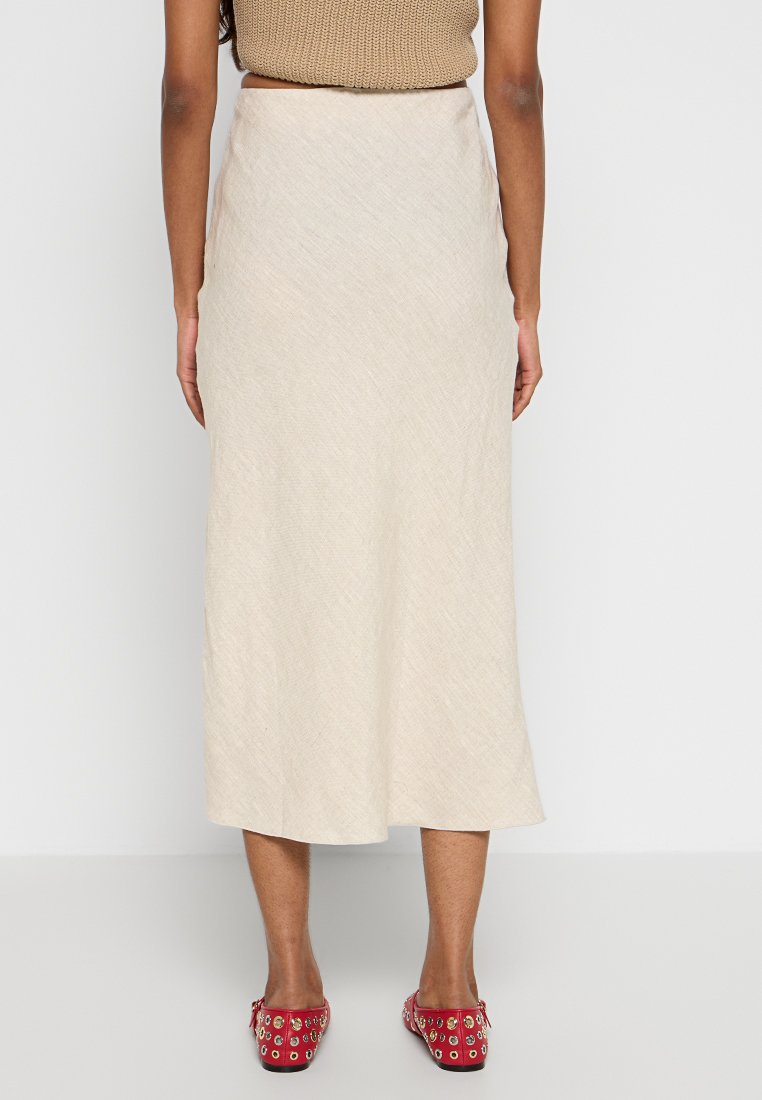 Beige Midikleid aus strukturiertem Stoff, mit einem ausgestellten Saum und einer glatten Silhouette. Kombiniert mit roten, beschlagenen Slippern.