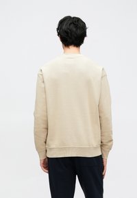 Beige sweatshirt met geribbelde manchetten en zoom, zachte textuur, ronde halslijn en losse pasvorm. Geen zichtbaar merk of opvallende patronen.