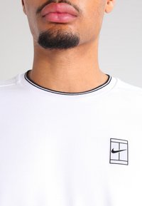 White cotton T-shirt with a round black and white striped neckline. Features a small black logo on the left chest area, smooth texture.