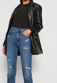 Svart läderblazer över en svart topp, kombinerad med blå slitna jeans. Jeanssen har revor och en klassisk design med fem fickor.