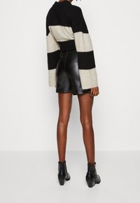 Černý a krémový pruhovaný svetr s texturovaným pletením, zkombinovaný s vysokými černými koženými šortkami a černými kotníkovými botami na podpatku.