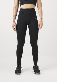 Leggings neri a vita alta realizzati in materiale elastico, con un design elegante caratterizzato da cuciture sagomate, abbinati a scarpe da ginnastica nere.