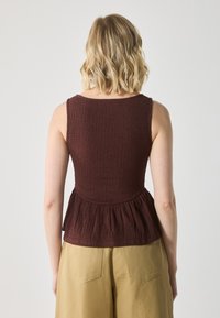 Bordo peplum tops ar teksturētu, krunkotu audumu. Tam ir apaļš kakla izgriezums un plašas plecu lences, apvienots ar gaiši pelēkām biksēm.