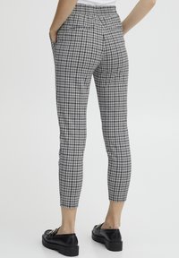Karirane hlače u crno-bijeloj boji, sa slim fit krojem, elastičnim strukom i bočnim džepovima, u kombinaciji s crnim robustnim cipelama.