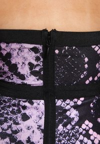 Černá a fialová látka s vzorem a se zipovým uzávěrem na zadní straně. Materiál má hladký povrch s abstraktními tvary a akcenty.