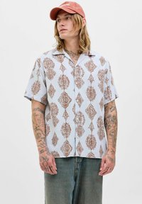 Chemise à manches courtes de couleur bleu clair avec un motif géométrique marron. Elle dispose d'un col boutonné et d'une coupe décontractée, fabriquée en tissu doux.