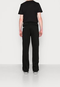 Zestaw składający się z czarnej koszulki i czarnych dresów, cechujący się luźnym krojem, dwoma kieszeniami z tyłu oraz białymi logo na spodniach.