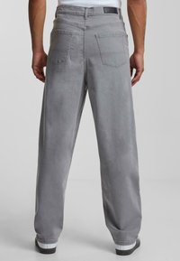 Gray denim jeans with a relaxed fit, featuring two back pockets and a stitched waistband label. The fabric has a soft texture.