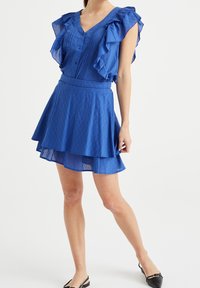 Niebieska sukienka z pionowymi paskami, falbaniastymi rękawami, dekoltem w kształcie litery V, dopasowanym talią i warstwową spódnicą z rozszerzanym dołem.