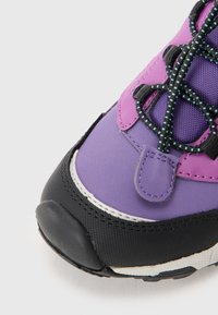 Lila och svart sneaker med en texturerad ovandel, kontrasterande snörning och förstärkt tå. Märkbara blanka detaljer på mellansulan.