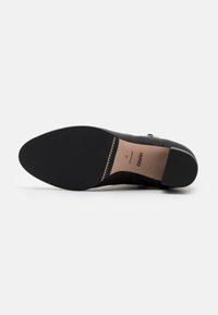Chaussures noires avec une tige en cuir lisse et une semelle extérieure en caoutchouc texturée. Elles présentent un design épuré avec une quincaillerie minimale et des accents subtils.