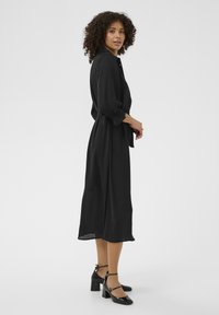 Czarna midi sukienka uszyta z lekkiego materiału, z kołnierzykiem, długimi rękawami z elastycznymi mankietami oraz paskiem do przewiązania w talii.