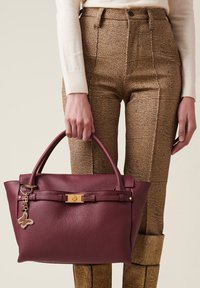 Borsa a mano in pelle bordeaux con design strutturato, hardware dorato e un portachiavi a forma di farfalla. Superficie testurizzata e manico superiore.