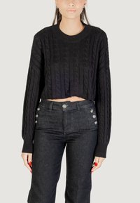 Pullover corto in maglia a trecce nera con maniche lunghe, abbinato a jeans in denim scuro a vita alta con bottoni decorativi in argento.