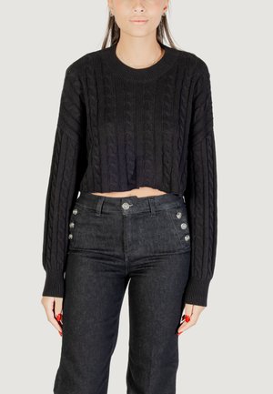 Pullover corto in maglia a trecce nera con maniche lunghe, abbinato a jeans in denim scuro a vita alta con bottoni decorativi in argento.
