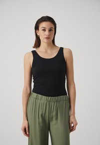 Black tank top made of flexible material, round neckline, paired with loose, green, high-waisted pants featuring an elastic waistband.