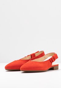 Red suede slingback shoes with a pointed toe, low block heel, and a decorative bow detail on the heel strap. Smooth interior lining.