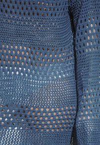 Tessuto lavorato a maglia blu con un design a rete caratterizzato da fori grandi e piccoli, creando un aspetto testurizzato con diverse sfumature di blu.