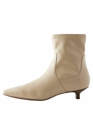 Beige ankle boot made of smooth leather with a slouched design, pointed toe, and a low, tapered heel. Stitch detailing at the top.