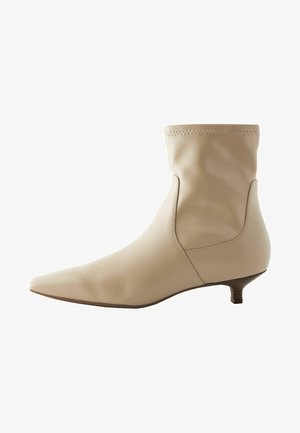 Beežid pahkluu saapad, mis on valmistatud siledast nahast, slouch-disainiga, terava ninaga ja madala, kitseneva kontsaga. Ülalt õmblustähtedega.