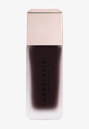 Hoge mat glazen fles met donkerbruine vloeistof en glanzende lichtroze dop, gelabeld als Anastasia Beverly Hills cosmeticaproduct.