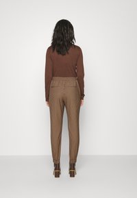 Haut marron à manches longues assorti à un pantalon à carreaux marron et beige avec taille et ourlet élastiques, porté avec des bottes à talons foncées.