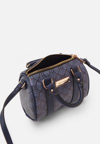 Piccola borsa a mano in materiale blu testurizzato con motivo geometrico, zip dorata e doppi manici in pelle. Presenta una tracolla regolabile per maggiore versatilità.