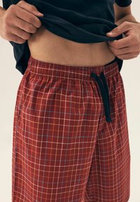 Czerwono-szachowe szorty z elastycznym pasem i czarnym sznurkiem. Wzór w kratkę zawiera niebieskie i żółte akcenty.