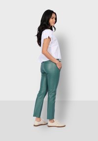 Top corto blanco de manga corta con mangas con volantes, combinado con pantalones ajustados de imitación cuero verdes y zapatillas blancas, mostrando un atuendo casual.