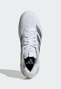 Vit sportig sko med en ovandel av mesh, grå ränder och en texturerad sula. Har snören och en Adidas-logotyp på tungan.