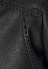 Texture en cuir synthétique noir avec un grain visible, mettant en valeur des détails de couture et des plis doux, créant une apparence lisse mais texturée.