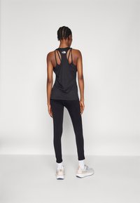 Svart tank topp med flerstrapedesign, kombinert med svarte leggings og grå sneakers. Glatt stoff og tettsittende silhuett. Ingen synlige logoer på leggings.