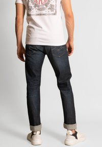 Mörkblå denimjeans med slim fit, med synliga sömmar, uppvikta fållar och två bakfickor med en subtil design.