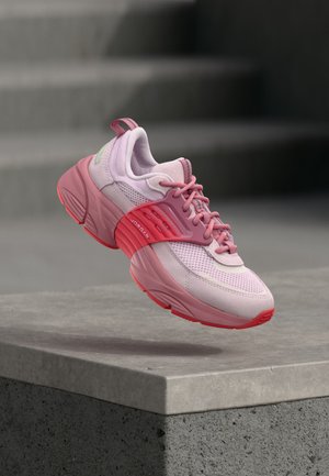Roze-rode Jordan sneaker zweeft boven een grijze stenen richel met wazige treden op de achtergrond.