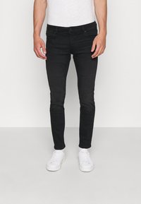 Černé slim-fit džíny vyrobené z denimu, s pěti kapsami, poutky na opasek a jemnými detaily šití, v kombinaci s bílými teniskami.