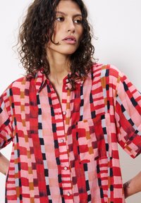 Kurzarmhemd aus leichtem Material mit einem geometrischen Muster in Rot, Rosa und Marineblau, Knopfleiste und einer Brusttasche.