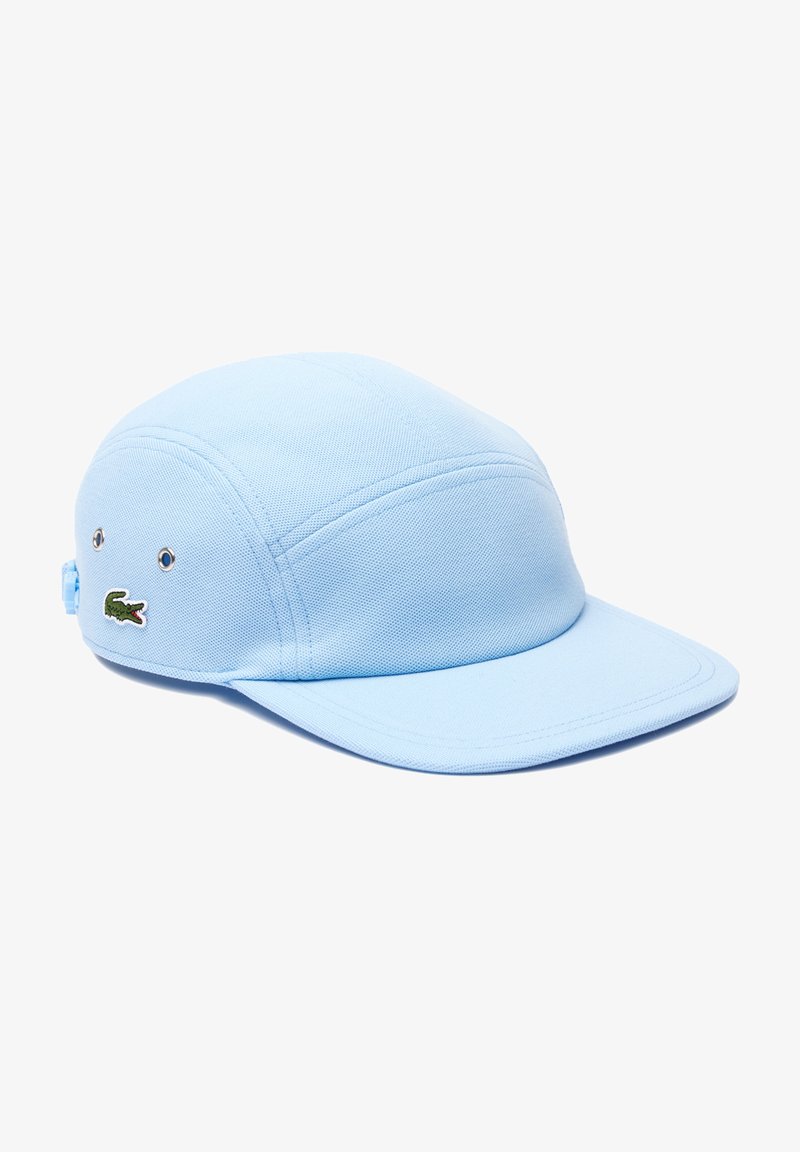Gorra azul claro hecha de tela texturizada, con una corona redondeada, visor plano y un logotipo de cocodrilo verde bordado en el lateral.