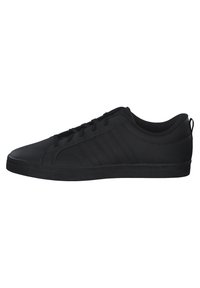Zapatos deportivos negros con parte superior de cuero suave, puntera redonda y suela de goma plana. Presenta tres rayas verticales en el costado.
