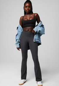 Schwarzes Cropped-Top, hellblaue übergroße Jeansjacke, graue ausgestellte Leggings, weiße Sneakers mit Gummisohlen. Einfaches Design, glatte Texturen.