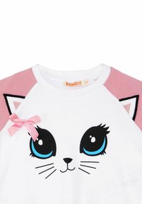 Camiseta blanca de algodón con mangas raglán rosas, que presenta un gráfico de cara de gato con grandes ojos azules, bigotes negros y un acento de moño rosa.