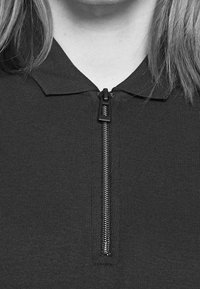 Haut à fermeture éclair de couleur gris foncé avec une texture côtelée, un col et une fermeture éclair à l'avant. Le design est simple et ajusté.