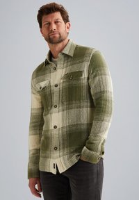 Geruite flanellen overhemd in groen en roomkleur, met een knoopsluiting aan de voorkant, twee borstzakken en een gestructureerde stof. Accenten omvatten donkere knopen.