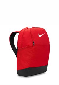 Czerwony plecak z tkaniny o zaokrąglonym kształcie, z czarnym dnem, podwójnymi zamkami i białym logo Nike z przodu. Wygodne, wyściełane szelki.