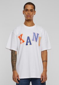 White cotton T-shirt with a loose fit, featuring multicolored letters "KANI" in orange, blue, and purple. Short sleeves, crew neck design.