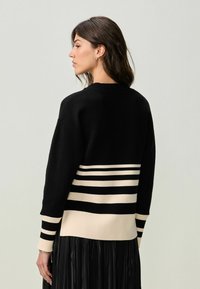 Pull noir en laine avec un col côtelé et un motif rayé en beige. Le design inclut de larges rayures à l'ourlet et aux manches.