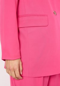 Fioletowy blazer o gładkiej fakturze, z pojedynczym guzikiem i boczną kieszenią. Prezentuje dopasowany krój i długie rękawy.