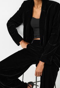 Czarny aksamitny garnitur z dopasowaną górą o prążkowanej fakturze oraz skrojoną marynarką z klapami, w zestawie z szerokimi spodniami.