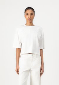 Witte cropped t-shirt met korte mouwen, met textuur en bloemenborduursel op de voorkant. Gepaard met witte high-waisted jeans.